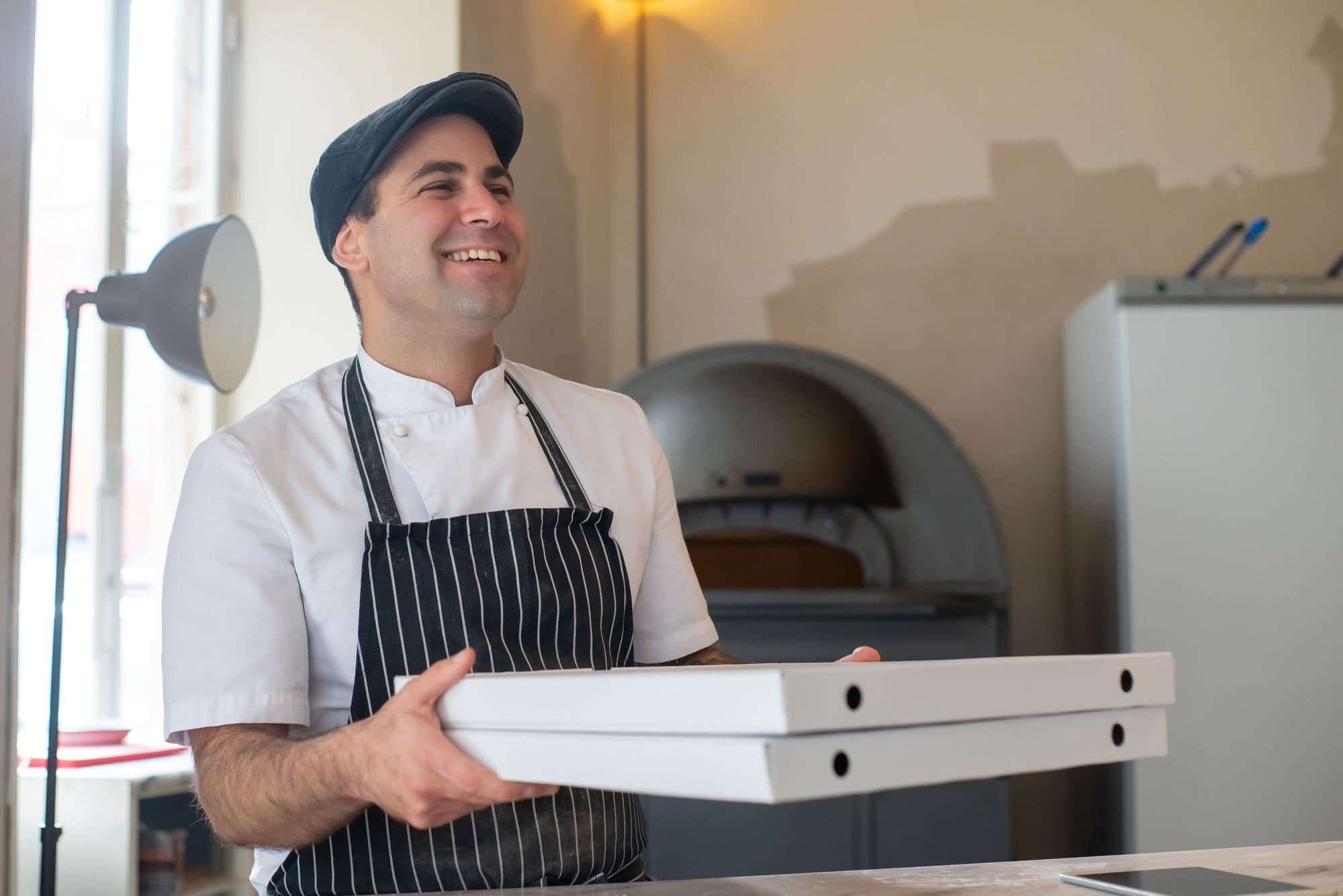 Un pizzaiolo sorride con due cartoni di pizza in mano.