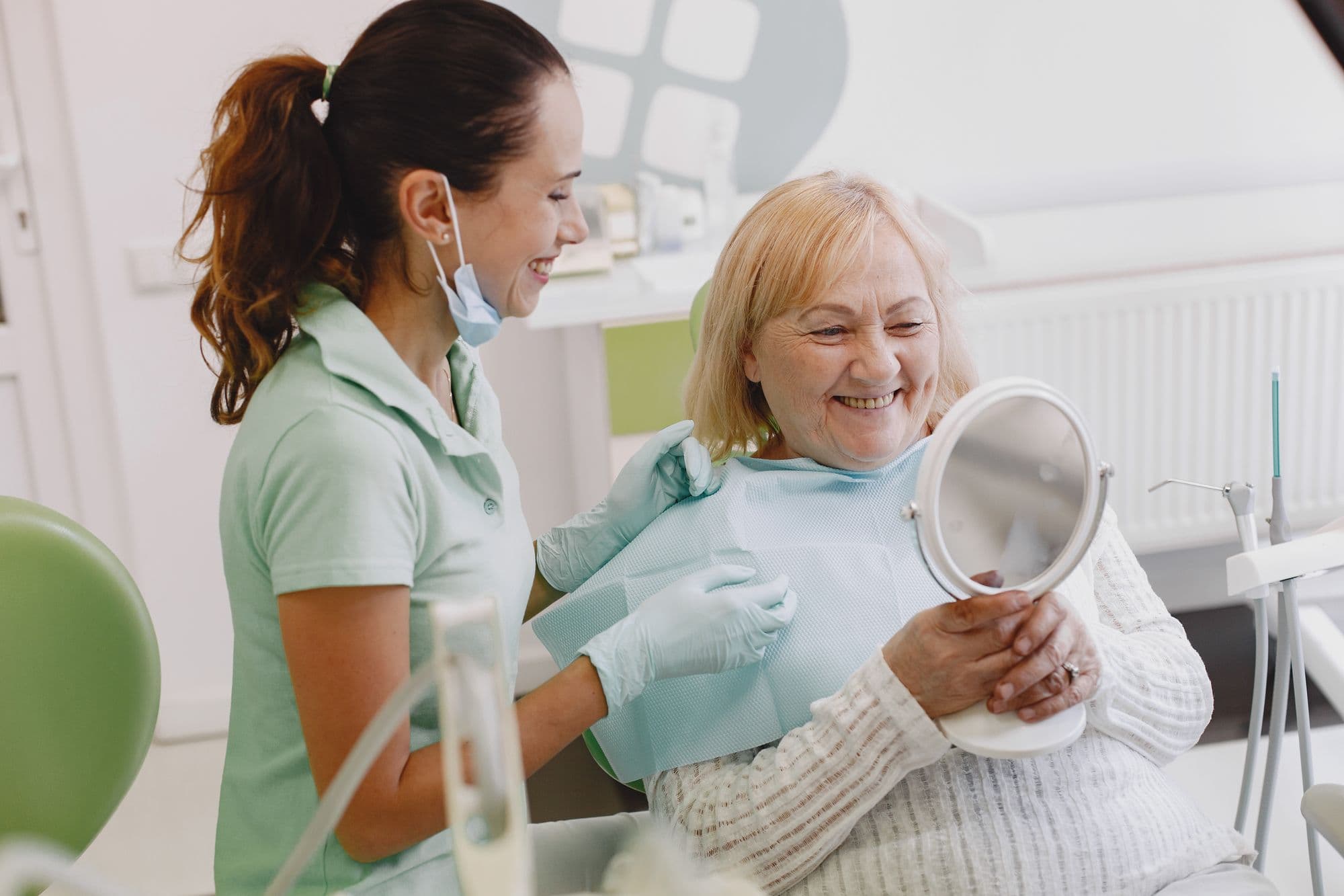 Una dentista e una paziente sorridono guardando uno specchietto.